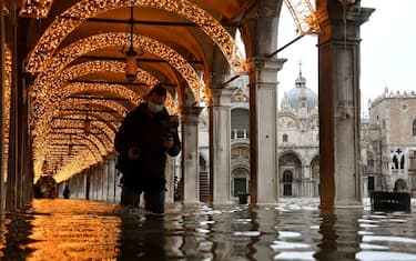 TOPSHOT - A man walks across an arcade by a flooded St. Mark's Square on December 8, 2020 in Venice following a high tide "Alta Acqua" event following heavy rains and strong winds, and the mobile gates of the MOSE Experimental Electromechanical Module that protects the city of Venice from floods, were not lifted (Photo by ANDREA PATTARO / AFP) (Photo by ANDREA PATTARO/AFP via Getty Images)