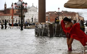 TOPSHOT - A view shows a model holding her dress on a flooded St. Mark's Square on December 8, 2020 following a high tide "Alta Acqua" event following heavy rains and strong winds, and the mobile gates of the MOSE Experimental Electromechanical Module that protects the city of Venice from floods, were not lifted. (Photo by ANDREA PATTARO / AFP) (Photo by ANDREA PATTARO/AFP via Getty Images)