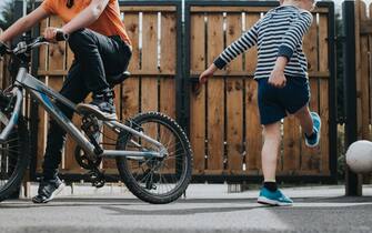 Two young boys in lockdown keep fit in their back yard. One plays football and the other attempts to cycle in a constricted area. Space for copy.