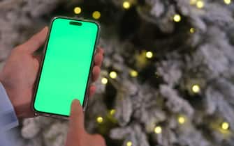 close up hand tapping green screen smartphone beside Christmas tree at night