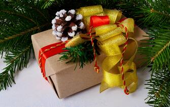 Christmas background with kraft paper wrapping Christmas present. Christmas gift box with golden bow and snowy pine cone.