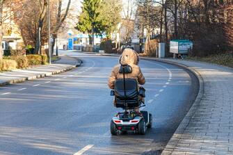 A disabled woman is riding her electric wheelchair on a cycle path next to the road.