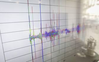 Shallow depth of field (selective focus) details with spikes on a seismogram on a digital display with the reflection of a device on the right.