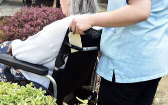 A care assistant pushes an elderly lady in her wheelchair anonymous view