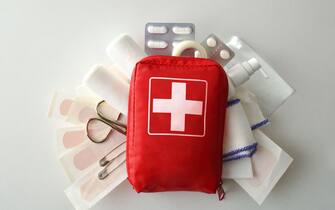 Travel portable first aid bag full of objects and tools for minor cures on white table. Top view. Horizontal composition