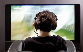 Teenager (15 years) sitting in chair shot from behind in studio playing video game on flat screen TV New York USA.
