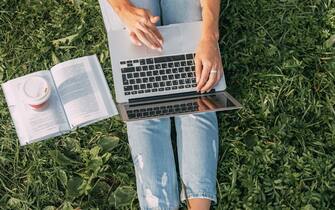 Top view of a laptop on the legs of a girl sitting in the park on the grass. Freelancer at work. Girl communicates online and watches webinars