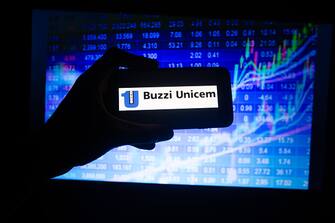 The logo of the Italian company Buzzi Unicem listed in the MIB in Milan is seen on a screen. In the background there is a colorful stock exchange price performance. (Photo by Alexander Pohl/NurPhoto via Getty Images)