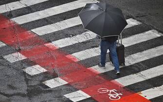 Un uomo cammina sotto l'ombrello dopo il nubifragio, Genova, 28 agosto 2023. (maltempo, ombrello, pedone, pedoni, strisce pedonali, attraversamento) ANSA/ LUCA ZENNARO