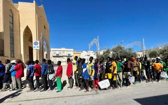 Alcuni migranti in fila per ricevere un pasto dalla Chiesa Parrocchiale di San Gerlando a Lampedusa, 14 settembre 2023. ANSA/ELIO DESIDERIO