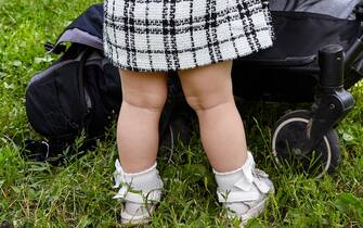 Baby pushing a stroller on a walk in summer park. Adorable little girl near pushchair and waiting for mom