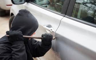 A robber dressed in black holding crowbar at a driver in a car. Car thief, car theft concept.