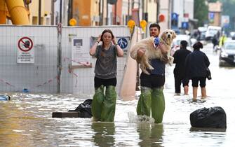 Pedestrians hold their dog in a flooded street in the town of Lugo on May 18, 2023, after heavy rains caused flooding across Italy's northern Emilia Romagna region. Rescue workers searched on May 18, 2023 for people still trapped by floodwaters in northeast Italy as more residents were evacuated after downpours which killed nine people and devastated homes and farms. (Photo by Andreas SOLARO / AFP) (Photo by ANDREAS SOLARO/AFP via Getty Images)