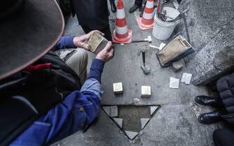 German artist Gunter Demnig puts three 'Snublesten' (Stolpersteine in German) in front of the via Baretti 31 in Turino, il 12 January 2023.  A stumbling block is a memorial stone laid in the pavement next to houses where victims of Nazism had their homes. ANSA/JESSICA PASQUALON