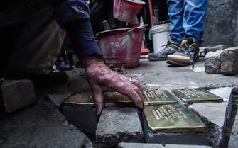 German artist Gunter Demnig puts three 'Snublesten' (Stolpersteine in German) in front of the via Baretti 31 in Turino, il 12 January 2023.  A stumbling block is a memorial stone laid in the pavement next to houses where victims of Nazism had their homes. ANSA/JESSICA PASQUALON