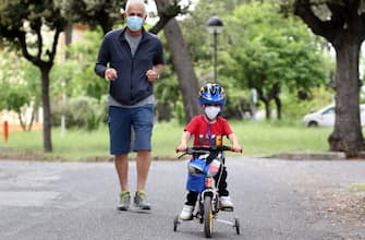 ROME, ITALY - MAY 12: The nephew of the photographer wears a face mask as he rides his bike along with his grandfather on May 12, 2020 in Rome, Italy. Italy was the first country to impose a nationwide lockdown to stem the transmission of the Coronavirus (Covid-19). (Photo by Elisabetta A. Villa/Getty Images)