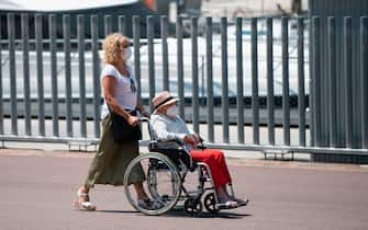 A woman pushes another one in a wheelchair in Barcelona's harbour, on July 18, 2020. - Four million residents of Barcelona have been urged to stay at home as virus cases rise, while EU leaders were set to meet again in Brussels, seeking to rescue Europe's economy from the ravages of the pandemic. (Photo by Josep LAGO / AFP) (Photo by JOSEP LAGO/AFP via Getty Images)