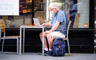 NEW YORK, NEW YORK - AUGUST 26: A person wears a protective face mask while working on a laptop at an outdoor dining area in the East Village as the city continues Phase 4 of re-opening following restrictions imposed to slow the spread of coronavirus on August 26, 2020 in New York City. The fourth phase allows outdoor arts and entertainment, sporting events without fans and media production. (Photo by Noam Galai/Getty Images)
