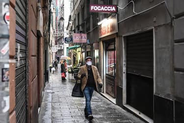 A resident wearing a protection mask carrying a shopping bag walks past typical food shops in the maze of alleys (Caruggi) of historic Genoa, Liguria, on March 13, 2020 as Italy shut all stores except for pharmacies and food shops in a desperate bid to halt the spread of a coronavirus. (Photo by Marco BERTORELLO / AFP) (Photo by MARCO BERTORELLO/AFP via Getty Images)