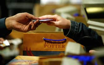 A shopkeeper takes a credit card as a Harry Potter fan buys a copy of "Harry Potter and the Order of the Phoenix" after the long awaited fifth book in the Harry Potter series became available, 21 June 2003, at London's King's Cross rail station. The much-anticipated book went on sale across the world at midnight UK time 21 June amid upprecedented fanfare.  King's Cross Station in the novel is where the young wizard catches the Hogwarts Express to school from Platform 9-3/4 .   AFP PHOTO/ODD ANDERSEN  (Photo credit should read ODD ANDERSEN/AFP via Getty Images)