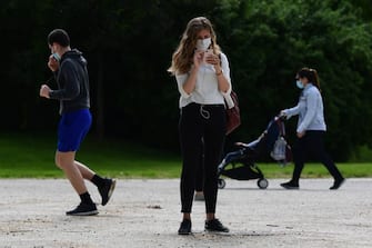 A woman checks her smartphone in the Parco Sempione park on May 4, 2020 in Milan as Italy starts to ease its lockdown, during the country's lockdown aimed at curbing the spread of the COVID-19 infection, caused by the novel coronavirus. - Stir-crazy Italians will be free to stroll and visit relatives for the first time in nine weeks on May 4, 2020 as Europe's hardest-hit country eases back the world's longest nationwide coronavirus lockdown. (Photo by Miguel MEDINA / AFP) (Photo by MIGUEL MEDINA/AFP via Getty Images)