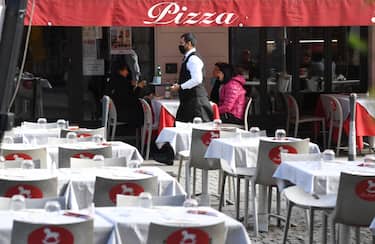 A waiter, wearing a face mask, walks past the only occupied by clients table terrace in a restaurant in the center of Milan, Italy, 27 October 2020. Smartworking, now used by many companies as a Covid containment measure, is impacting dramatically on the catering economy.ANSA/DANIEL DAL ZENNARO