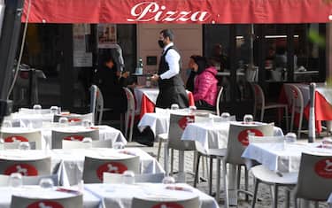 A waiter, wearing a face mask, walks past the only occupied by clients table terrace in a restaurant in the center of Milan, Italy, 27 October 2020. Smartworking, now used by many companies as a Covid containment measure, is impacting dramatically on the catering economy.ANSA/DANIEL DAL ZENNARO