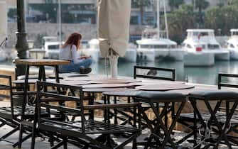 epa08798438 A girl sits outside a closed cafe at the Piraeus port, Greece, 04 November 2020. Greek government has decided that all cafes and restaurants will be closed in all high risk regions all over the country in order to stem the spread of the coronavirus (Covid-19) disease. Greece has been experiencing a rising rate of coronavirus infections, authorities said, with 26 regions in 'red alert', particularly in Thessaloniki and Serres, which were placed under full lockdown for the next two weeks.  EPA/PANTELIS SAITAS