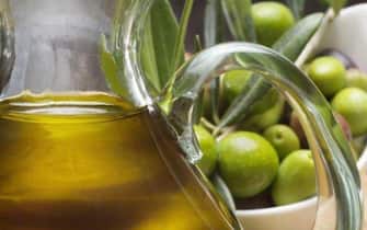 Un contenitore di olio in primo piano e olive verdi in secondo piano