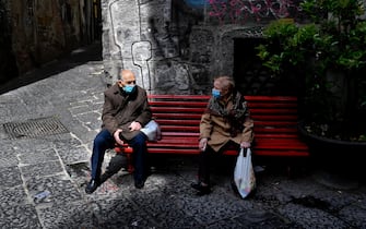 Anziani, indossando mascherine anti contagio,  si riposano su una panchina Rossa, simbolo della lotta alla Violenza sulle donne, nel centro antico di Napoli, 21  aprile   2021
 ANSA/CIRO FUSCO