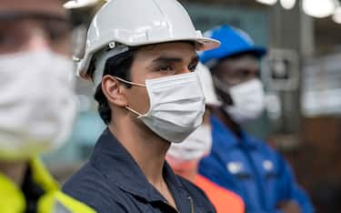 Shot of Multi-ethnic in heavy industry workers wearing face mask, helmet and jumpsuit. Focus on maintenance engineer.