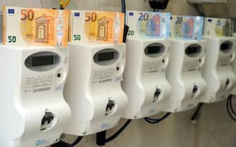 contatori luce con soldi simbolo del rincaro Milano - Aumento dei costi delle bollette della luce elettrica