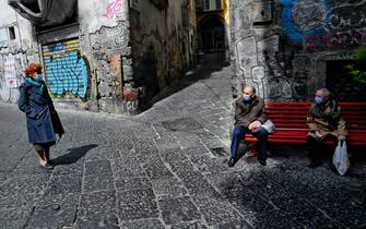 Anziani, indossando mascherine anti contagio,  si riposano su una panchina Rossa, simbolo della lotta alla Violenza sulle donne, nel centro antico di Napoli, 21  aprile   2021
 ANSA/CIRO FUSCO