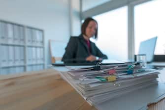 Busy businesswoman doing paperwork in office at the desk filled with papers and documentation