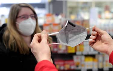 epa08958384 Pharmacist Stephan Neuhaus demonstrates the usage of a FFP2 protective mouth-nose mask with grey fleece to a customer at the Baeren pharmacy in Dortmund, Germany, 22 January 2021. In Germany, medical face masks will in future have to be worn on public transport, when shopping and even at religious services. To protect themselves more effectively, surgical masks or mouth-nose protection with the standards KN95/N95 or FFP2 will be required. People over 60 and people with certain chronic diseases will receive two vouchers for six FFP2 masks each from their health insurers and can redeem them at the pharmacy for a fee of two euros each.  EPA/FRIEDEMANN VOGEL