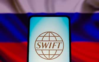 In this photo illustration, the Society for Worldwide Interbank Financial Telecommunication (SWIFT) logo is displayed on a smartphone with a flag of Russia in the background,
