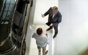 High angle view of a salesperson using touchpad while talking to his male customer in a car showroom. Copy space.
