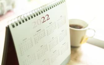 Paper desktop calendar 2022 schedule with tea cup on wooden desk