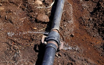 Water dripping from a leaky pipe in farm land. Water flows from a rusty pipe. Constant stream of water coming from a pipe. or Water bursts out of a leaking plumbing pipe laid on the ground