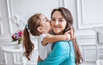 little girl about 10 years old embracing and kissing her smiling beautiful mother both looking at camera, happy family