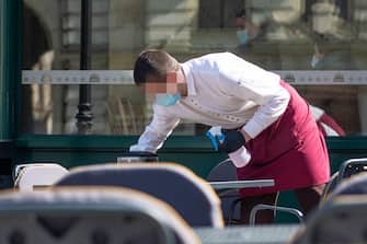Waiter with a mask disinfects the table of an outdoor bar, café or restaurant, reopen after quarantine restrictions