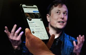 US-INTERNET-TWITTER-MUSK In this photo illustration, a phone screen displays the Twitter account of Elon Musk with a photo of him shown in the background, on April 14, 2022, in Washington, DC. - Tesla chief Elon Musk has launched a hostile takeover bid for Twitter, insisting it was a "best and final offer" and that he was the only person capable of unlocking the full potential of the platform. (Photo by Olivier DOULIERY / AFP)