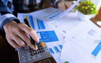 Close up businessman using calculator and reading paper document about business data, accountancy document, graph profit company.