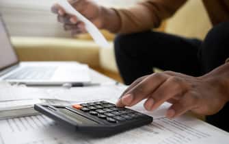 Close up of african american man with calculator checking bills at home. Savings, finances, economy concept. Black small business owner calculating income and planning budget
