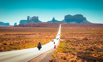 Classic panorama view of motorcyclist on historic U.S. Route 163 running through famous Monument Valley in beautiful golden evening light at sunset in summer, Utah, USA