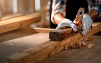 close up Hands of a asian male carpenter holding a draw knife and trimming a plank