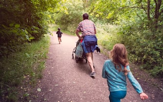 A father pushing a pushchair along a path through a country park with children running along with him.