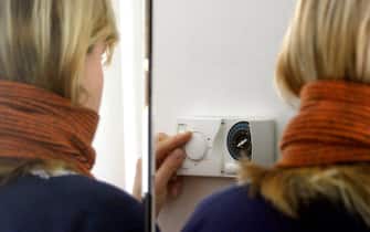 Una donna regola il termostato di un impianto di riscaldamento di una abitazione, in una immagine di archivio.
ANSA/FOLCO LANCIA