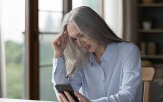 Angry nervous older businesswoman looking at smartphone screen