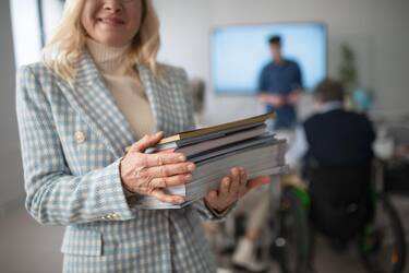 Happy senior woman student posing with books in classroom.